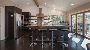 A modern kitchen with a central island, stainless steel appliances, and a large window overlooking a deck. - Skylake Serenity Retreat (Incline Village)