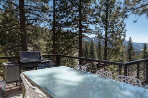 A balcony with a glass table and chairs, a barbecue grill, and a view of a forested mountain area. - Skylake Serenity Retreat (Incline Village)