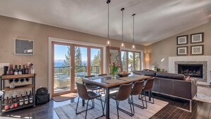 A spacious living room with a dining area, large windows, a fireplace, and a wine rack. - Skylake Serenity Retreat (Incline Village)