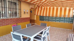 Een eethoek met een tafel, stoelen, een bakstenen muur en een gestreept zonnescherm.