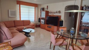 Een woonkamer met een bank, salontafel, televisie en een glazen eettafel met stoelen.