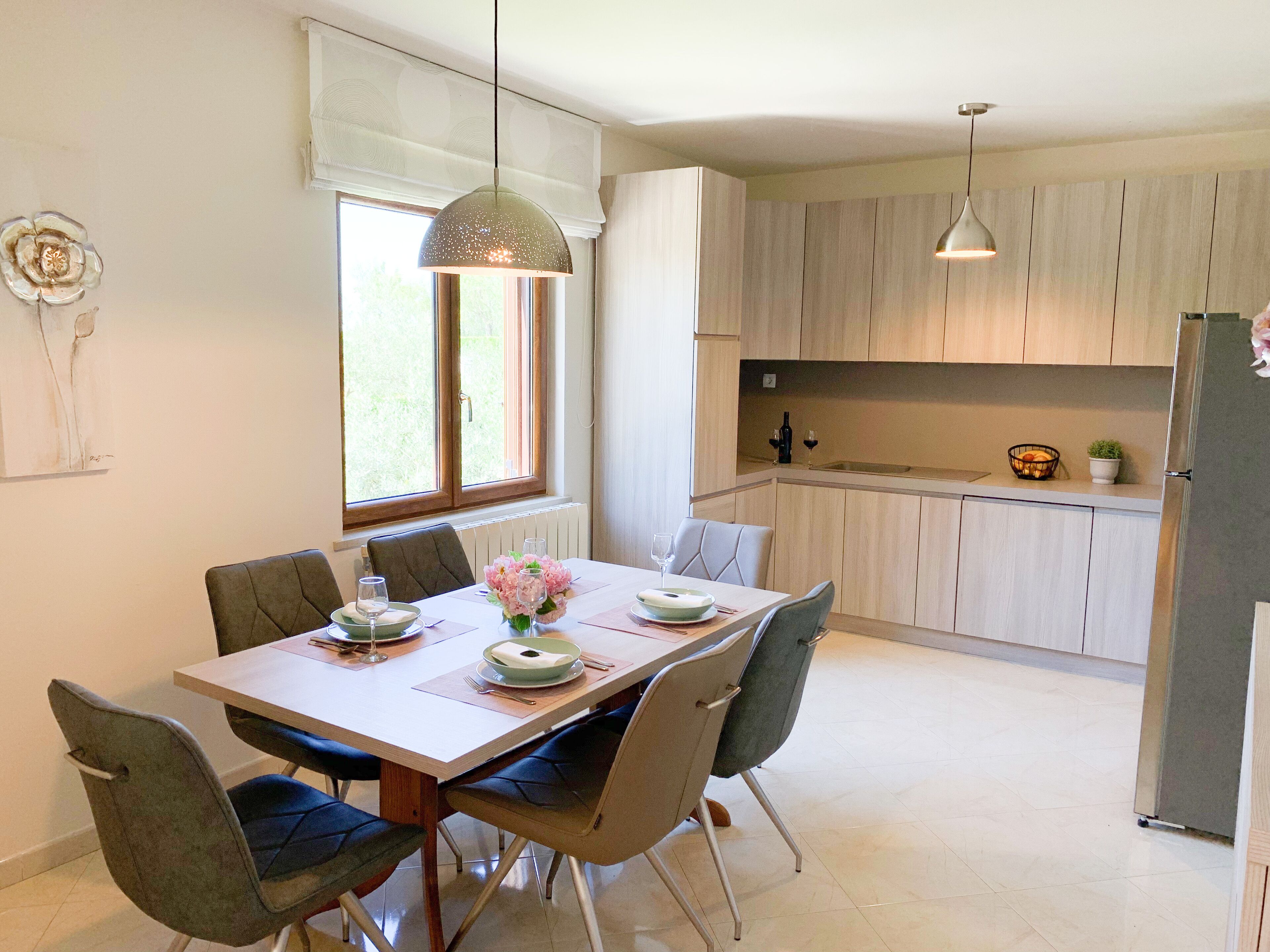 A modern kitchen with light wood cabinets, a stainless steel refrigerator, and a dining area with a table set for two.