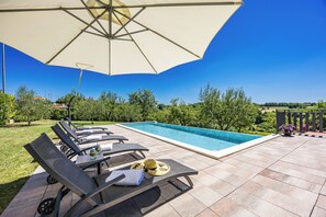 A poolside area with lounge chairs, a table with drinks, and a large umbrella. - Holiday Home with pool and garden (Pazin)