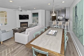 Una sala moderna con chimenea, un comedor con mesa de madera y una cocina con armarios blancos y una lámpara colgante.