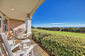 Un patio con mobiliario exterior y vistas a un césped cuidado y al océano.