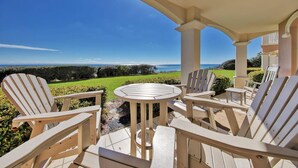 Estar coberto com mesa redonda e quatro cadeiras Adirondack, com vista para um jardim cuidado e para o oceano.