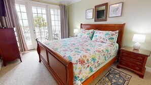 Un dormitorio con una cama de madera, ropa de cama floral, una mesita de noche, un aparador y vistas al exterior a través de una puerta corrediza de vidrio.
