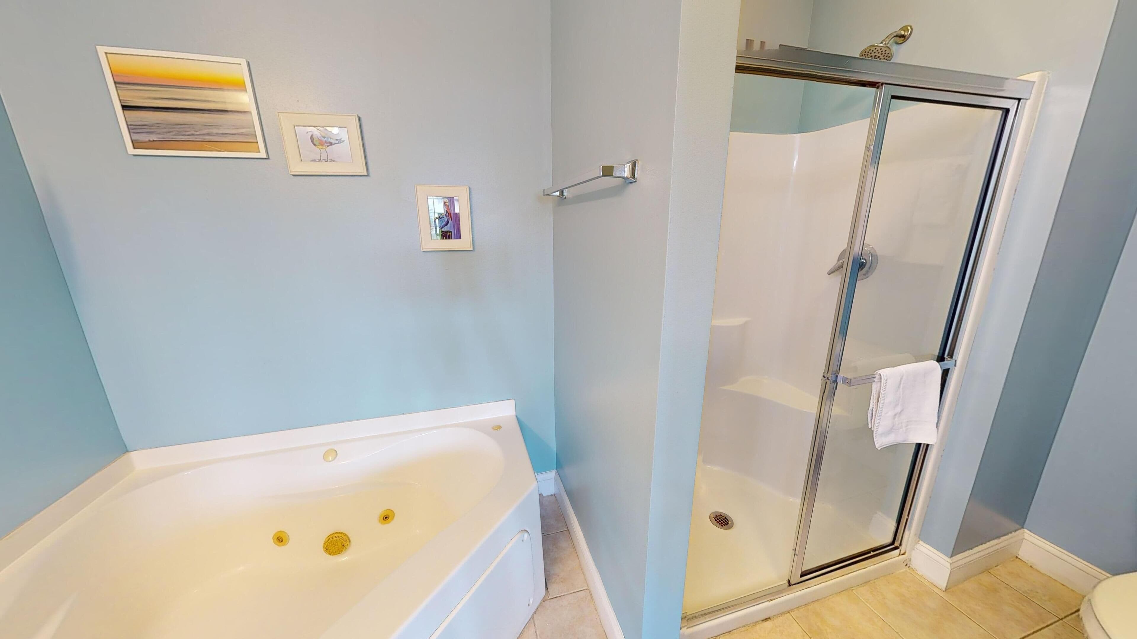 A bathroom with a bathtub, a glass-enclosed shower, and three framed pictures on the wall.