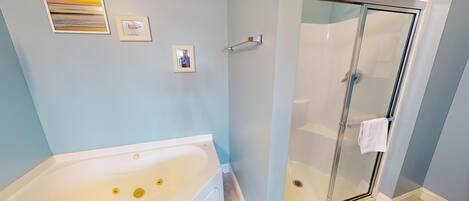 A bathroom with a bathtub, a glass-enclosed shower, and three framed pictures on the wall.