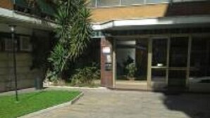 A paved walkway leading to a building entrance with a glass door and a small signboard. - Olimpica Relais Guest House Affittacamere CIR 28624 (Rome)