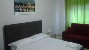 A hotel room with a bed, a nightstand, a red chair, a painting on the wall, and green curtains. - Olimpica Relais Guest House Affittacamere CIR 28624 (Rome)
