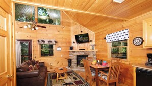 Un interior de cabaña acogedor, con detalles de madera, una chimenea, un televisor y una zona de comedor.