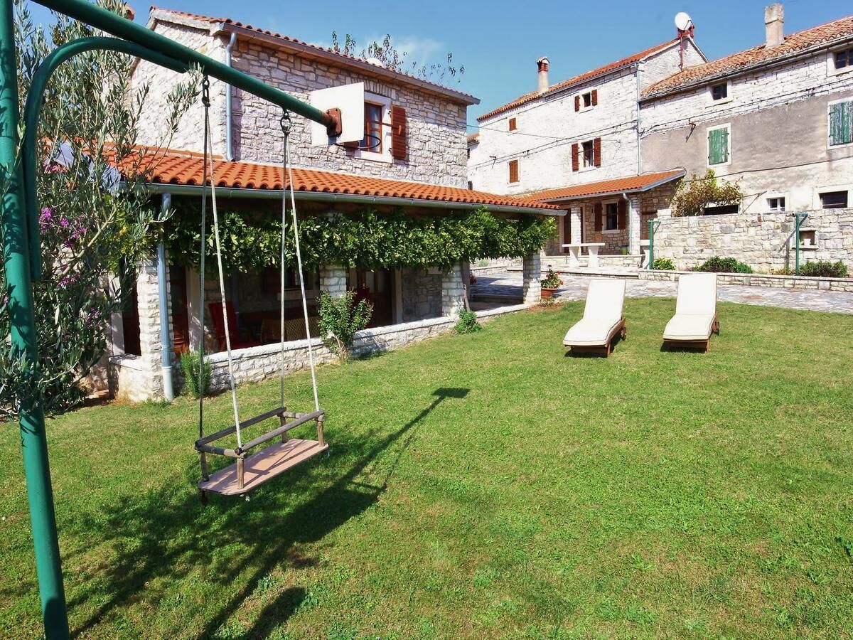 A stone building with a tiled roof, a swing set, and two lounge chairs.