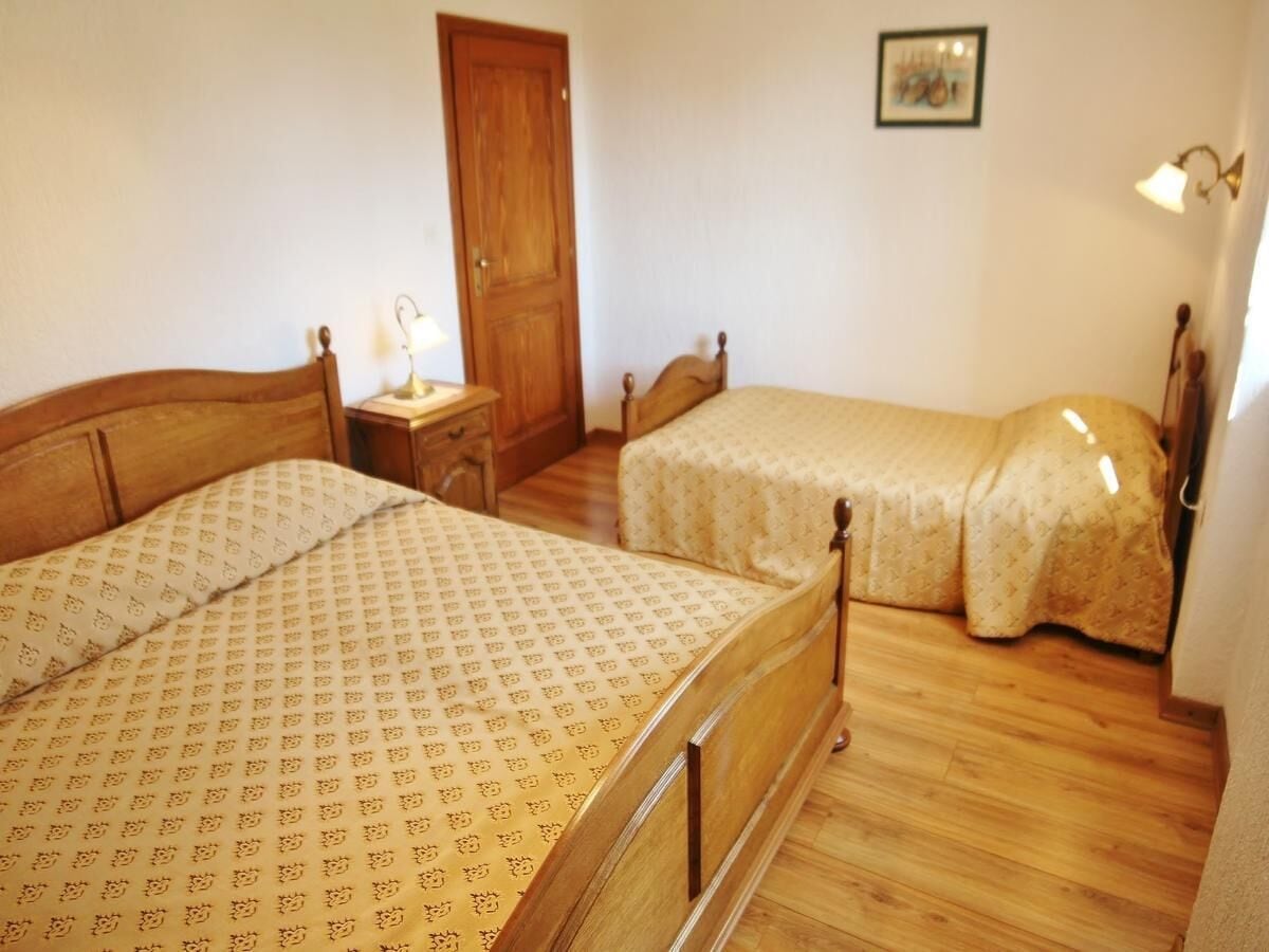 A bedroom with two wooden beds, a wooden wardrobe, a nightstand with a lamp, and a framed picture on the wall.