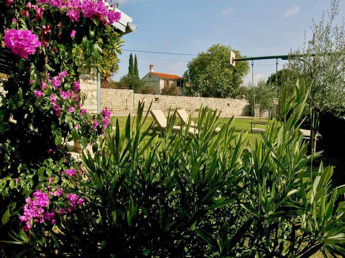 Um jardim com muro de pedra, baloiço e um edifício com telhado vermelho ao fundo.