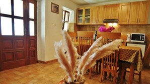 A kitchen with wooden cabinets, a dining table with chairs, a clock, and a vase with dried plants on the table. - Holiday Homes Ana & Maria (Kanfanar)