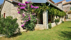 A stone house with a covered porch, surrounded by well-maintained grass and flowering plants. - Holiday Homes Ana & Maria (Kanfanar)