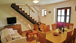A living room with a sofa, a dining table with chairs, a TV, a staircase, and a window. - Holiday Homes Ana & Maria (Kanfanar)