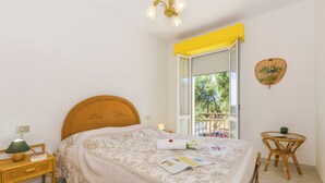Un dormitorio con cama, mesita de noche, lámpara y una pequeña mesa con una silla.
