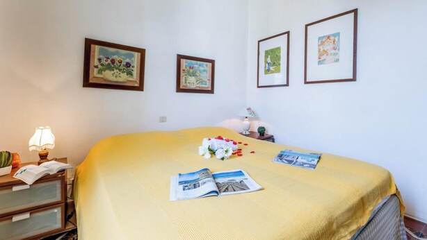 A neatly made bed with a yellow bedspread, a bedside table with a lamp, and three framed pictures on the wall. - Il Gladiolo - Focette 100mt From Sea (Pietrasanta)