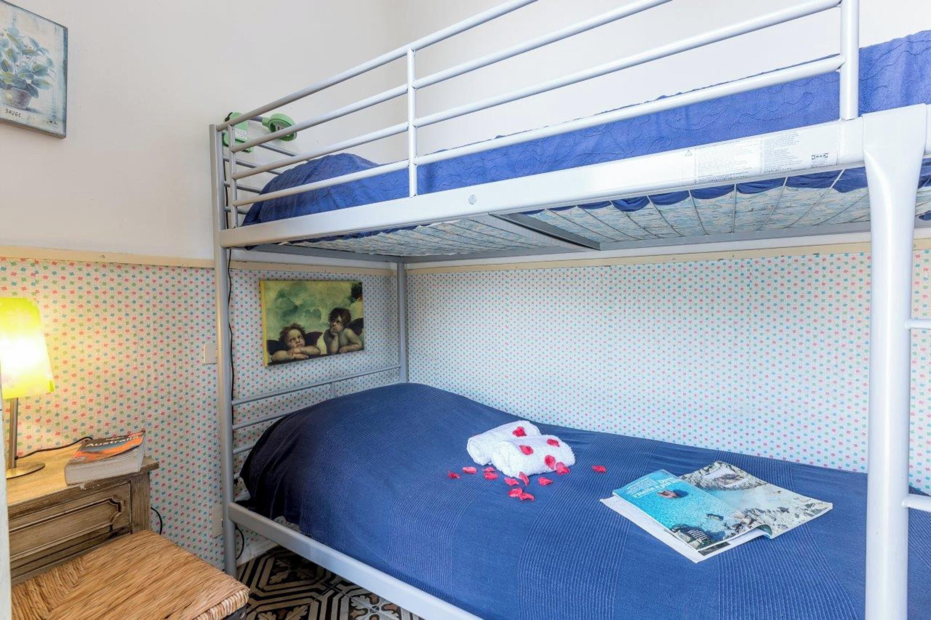 A bunk bed room with a blue mattress, a small bedside table with a lamp, and a polka dot wallpaper.