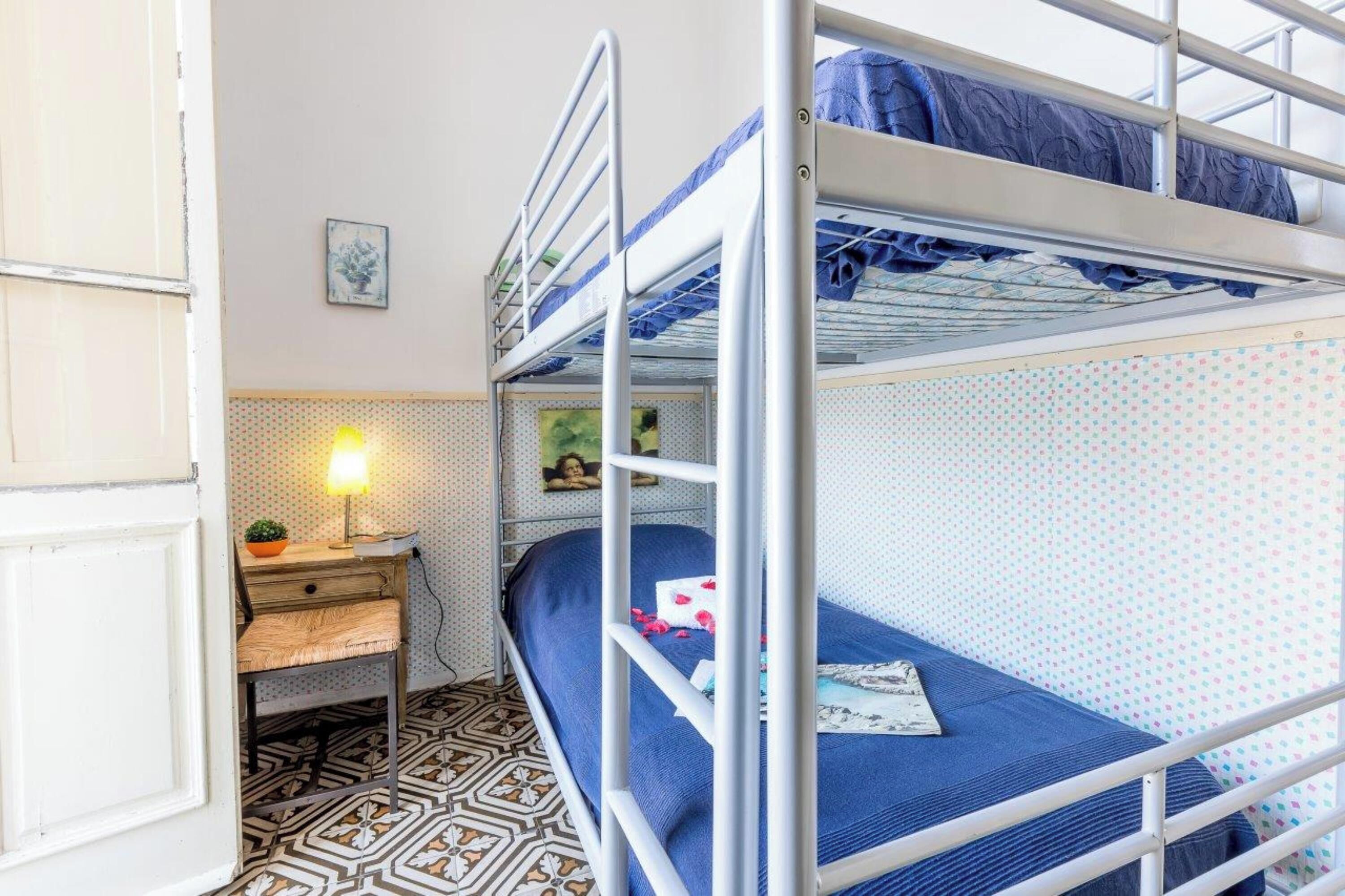 A bunk bed room with a patterned floor, a small desk with a lamp, and a framed picture on the wall.