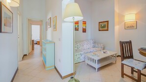 A living room with a sofa, a coffee table, a lamp, and a chair. There are framed pictures on the walls. - La Fresia - Focette 100mt From Sea (Pietrasanta)