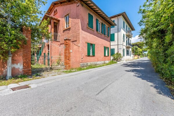 A narrow street lined with traditional buildings, a brick wall, and a metal gate. - La Rosa - Focette (Pietrasanta)