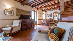 A cozy living room with a piano, wooden furniture, and a dining area with a table and chairs. - La Maggioletta (Massarosa)