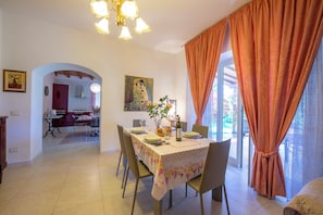 A dining area with a table set for four, a chandelier, and a view through the window. - Villa Clara few km from the sea (Pietrasanta)