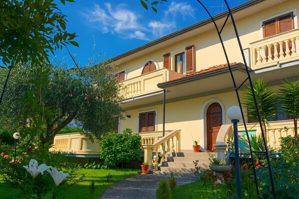 A two-story building with a balcony, a staircase, and a garden with flowers and plants.