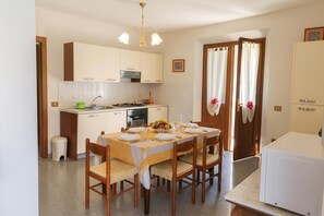 Une cuisine de taille réduite avec des meubles blancs, une table à manger pour quatre personnes et un réfrigérateur.