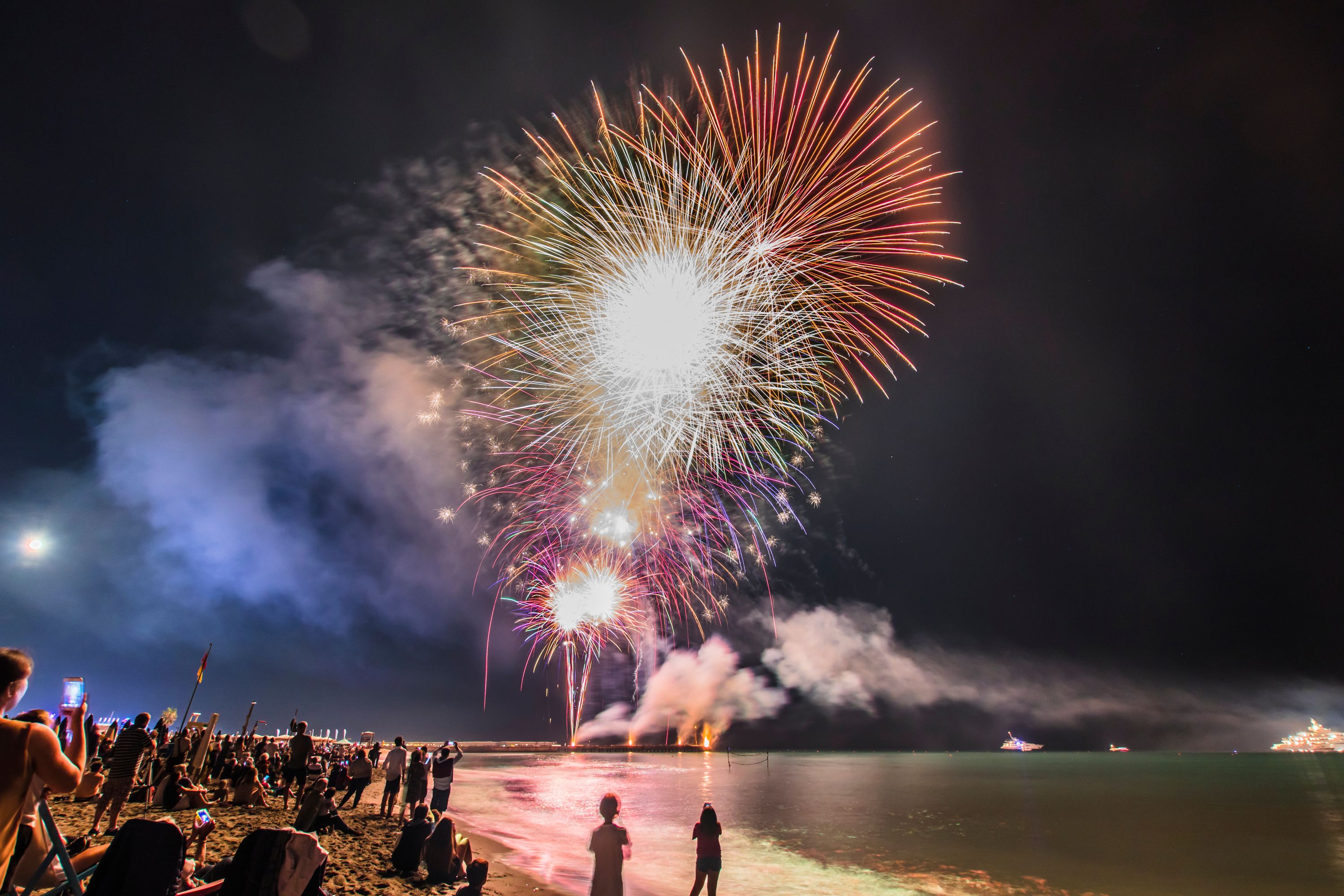 A beach with people watching fireworks.