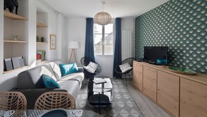 Un salon moderne avec un canapé, des fauteuils, une table basse et un téléviseur posé sur un meuble en bois.