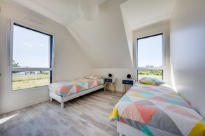 Ein Schlafzimmer mit zwei Betten, großen Fenstern und Blick auf ein Feld.