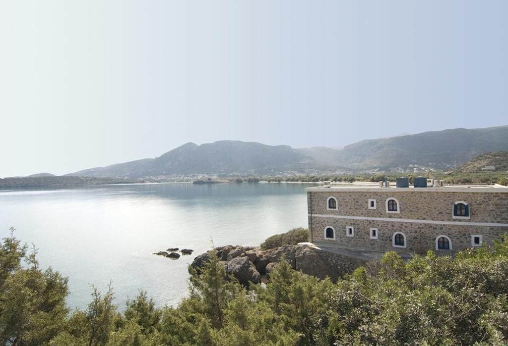A coastal building with a stone facade, overlooking a calm sea and distant hills.