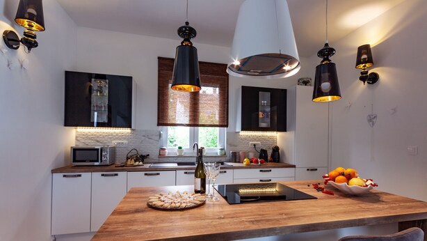 Cozinha moderna com ilha de madeira, armários brancos e iluminação pendente.