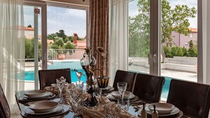 Mesa de jantar posta para quatro pessoas, com vista para uma piscina e edifícios ao fundo.