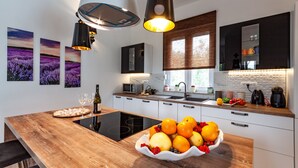 Cozinha moderna com ilha de madeira, luminárias pendentes pretas e uma tigela de frutas.