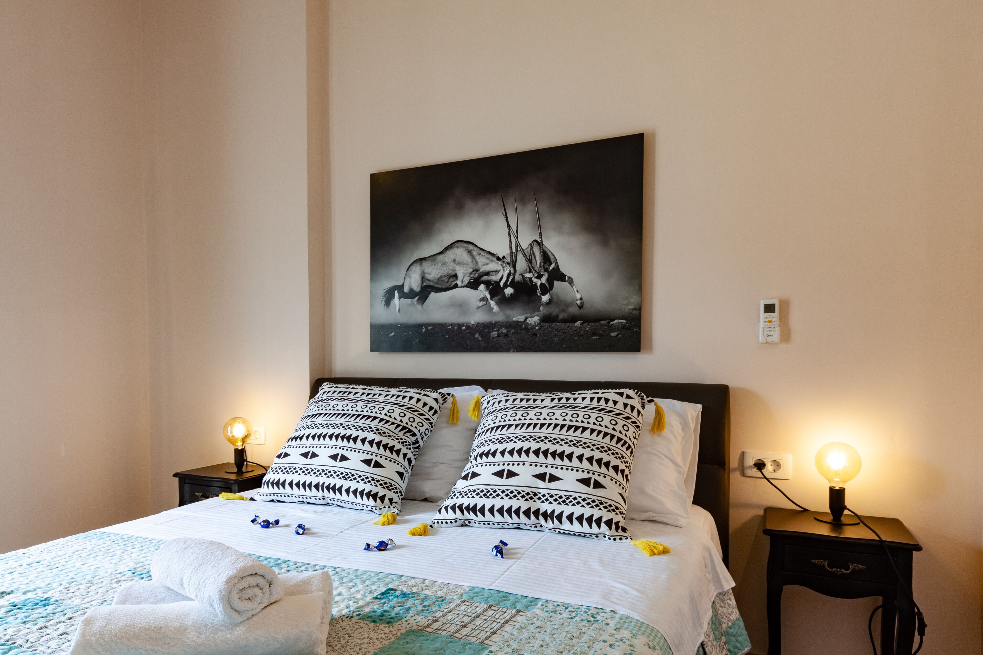 Una cama bien hecha con almohadas estampadas, una obra de arte en la pared con animales y lámparas de noche.