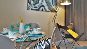 Et spiseområde med et bord dækket til fire personer, en moderne lampe og en stol med en gul pude.