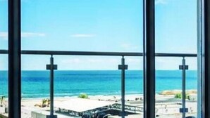 Blick aus einem Fenster auf einen Strand mit blauem Himmel.