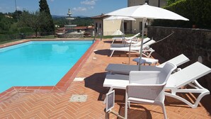 A swimming pool with lounge chairs and umbrellas, surrounded by a brick patio and a stone wall.