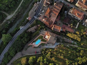 An aerial view of a residential area with a swimming pool, a road, and surrounding greenery.