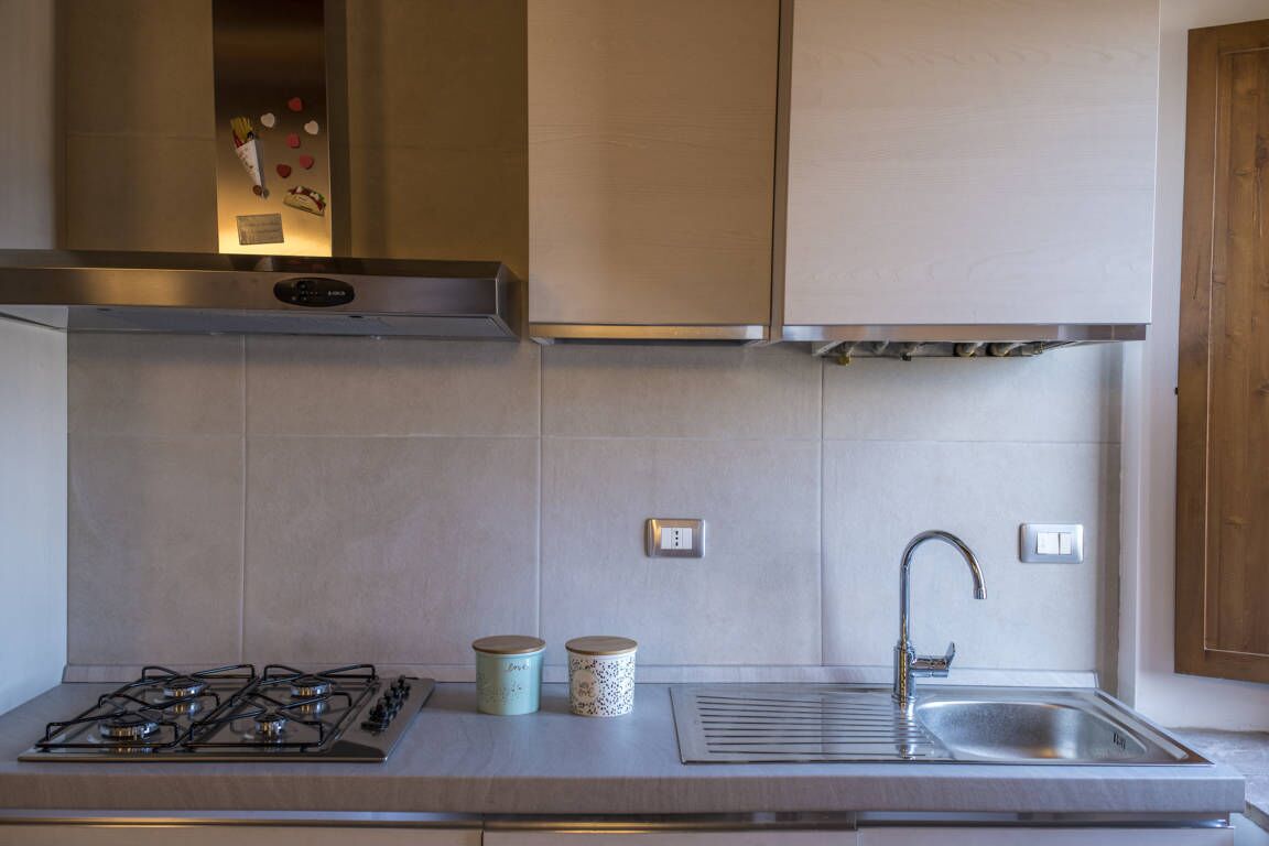 Una cocina con estufa a gas, pileta de acero inoxidable y baldosas de colores claros.