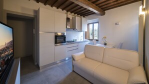 Una cocina moderna con armarios blancos, horno empotrado y una zona de comedor con sofá blanco.