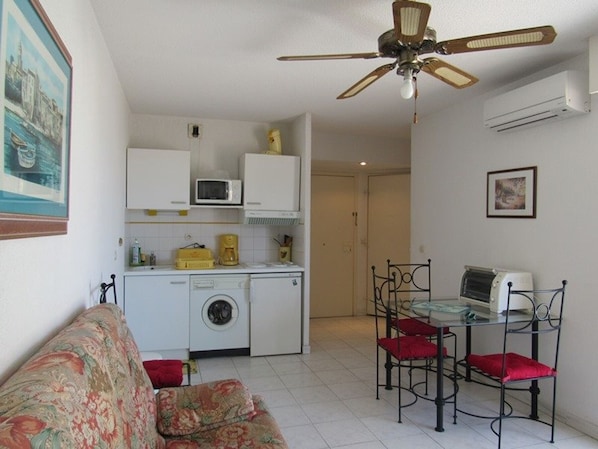 A compact living space with a kitchenette, a washing machine, a dining area with a table and chairs, and a ceiling fan.