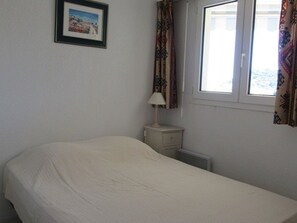 A bedroom with a bed, a nightstand, a lamp, a window with curtains, and a framed picture on the wall.