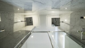A modern bathroom with marble walls and a glass floor, featuring a shower area and a sink.