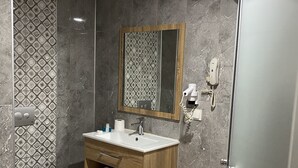 A modern bathroom with a marble-tiled floor, a wooden vanity with a mirror, a toilet, and a shower area.